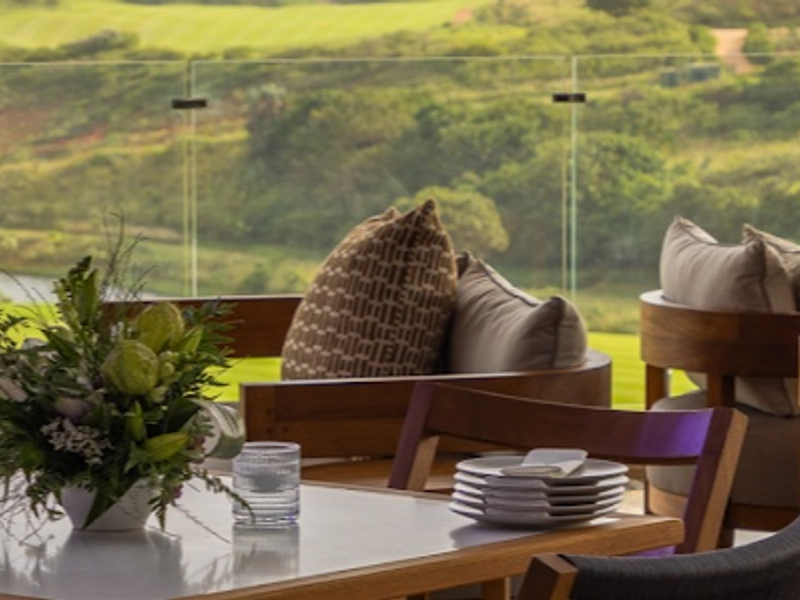 A scenic view overlooking a lush green landscape and water feature, framed by a modern glass balustrade.