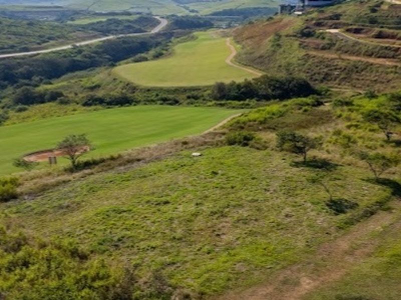 An aerial view of a vacant residential plot featuring sloped terrain and natural grassland, situated adjacent to a golf course landscape.