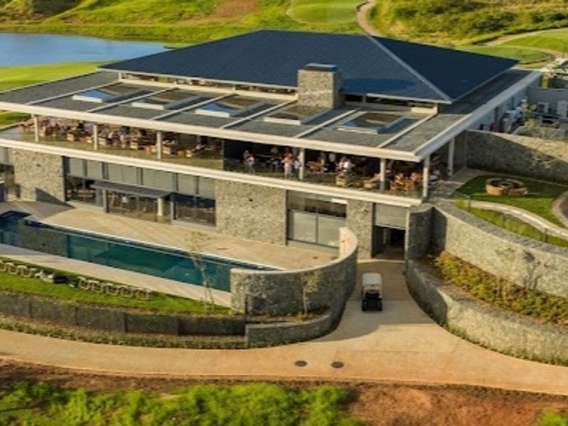 Aerial view of a modern clubhouse featuring stone exterior walls, a swimming pool, and extensive landscaped grounds within a golf estate.