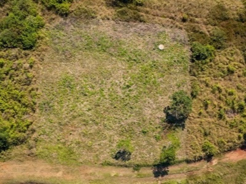 An aerial view of a vacant residential plot featuring cleared land surrounded by natural vegetation and an adjacent dirt access path.