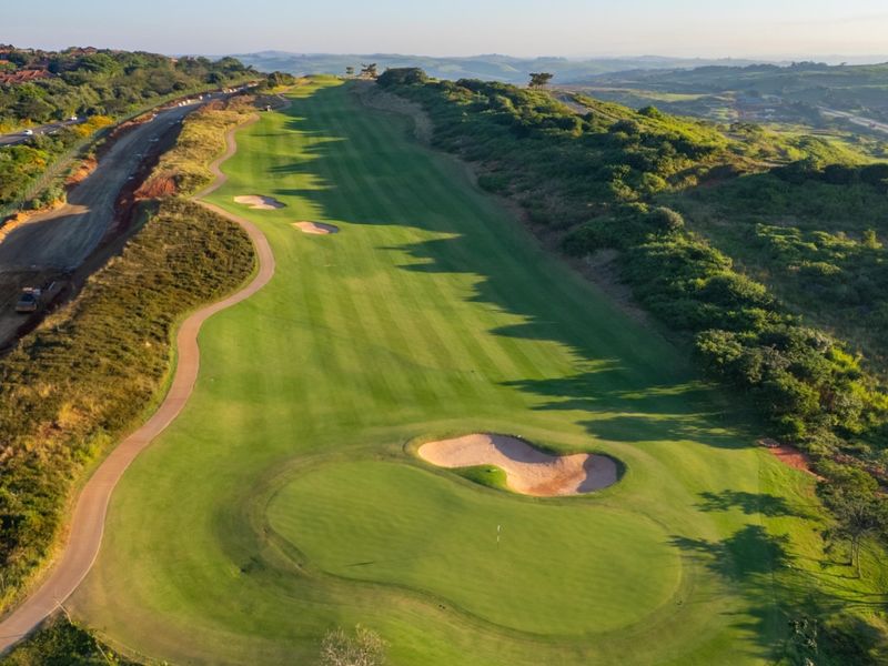 Aerial view of a well-maintained golf course fairway featuring sand bunkers and a paved cart path, set within a scenic landscape.