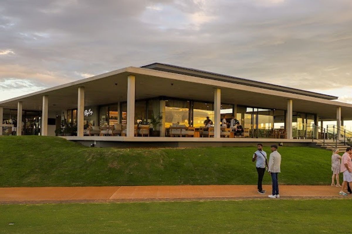 A modern architectural building featuring a spacious covered patio, large glass sliding doors, and expansive lawn area, ideal for outdoor entertainment.