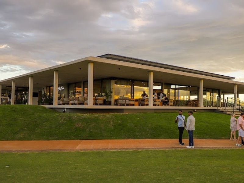 A modern architectural building featuring a spacious covered patio, large glass sliding doors, and expansive lawn area, ideal for outdoor entertainment.