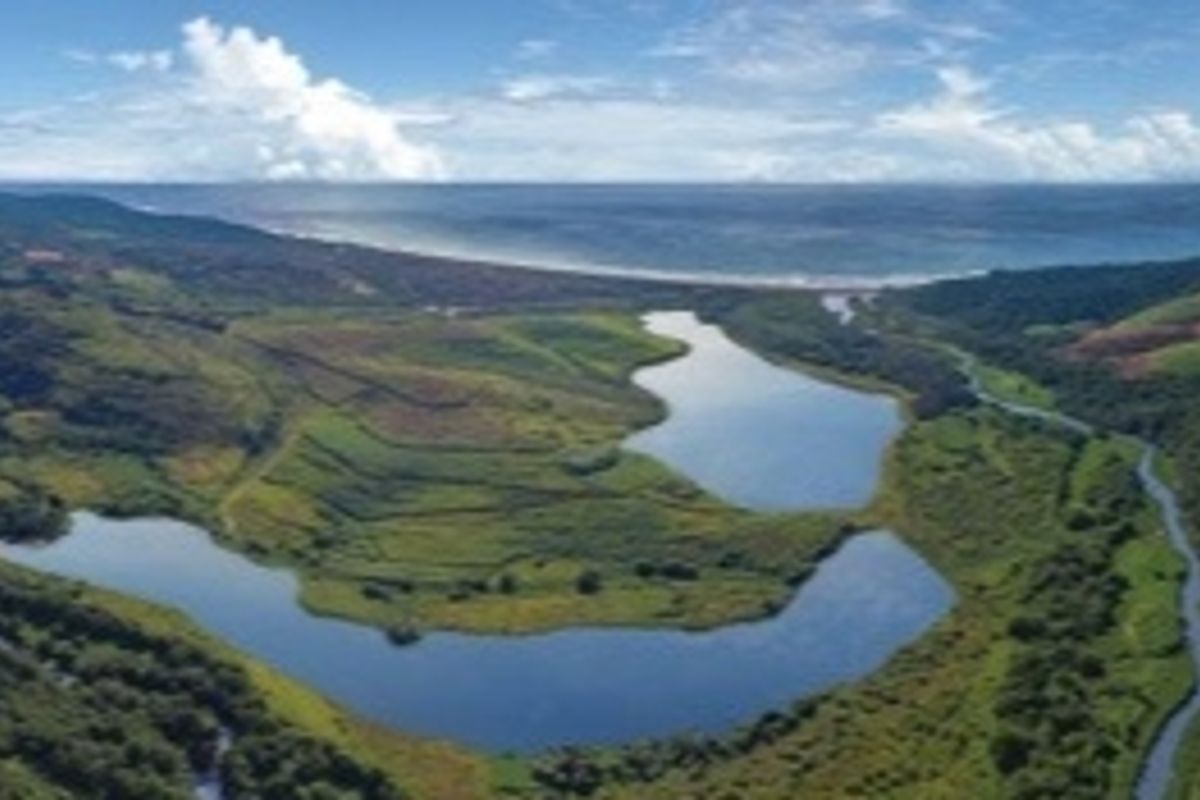 An aerial view of a scenic landscape featuring natural lakes, rolling green hills, and a distant coastline.