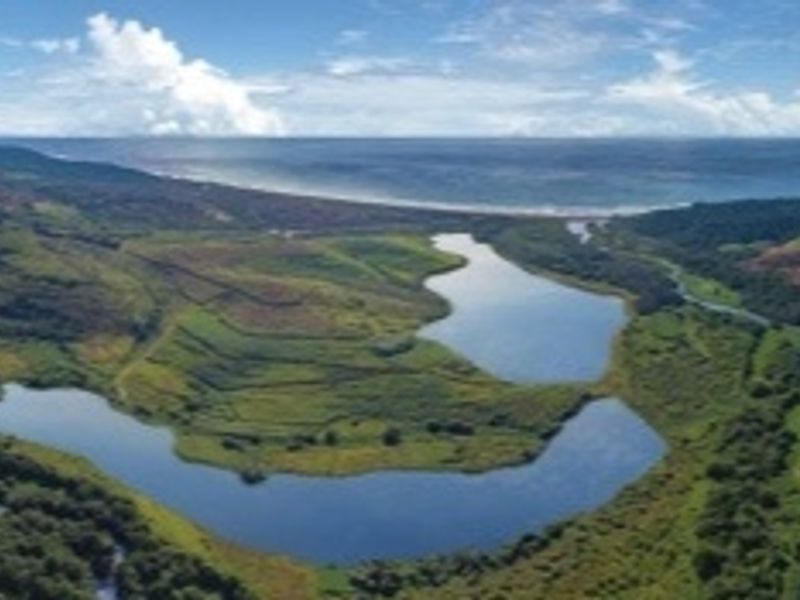 An aerial view of a scenic landscape featuring natural lakes, rolling green hills, and a distant coastline.