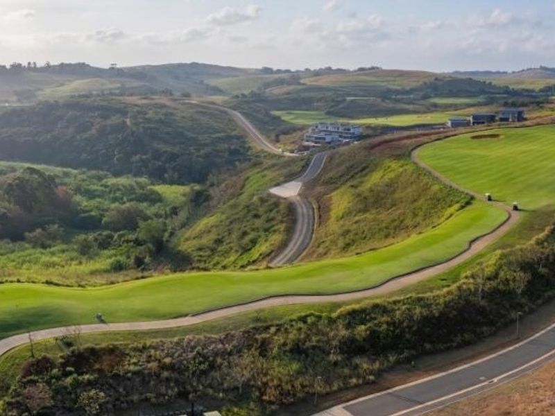 An aerial view of a residential estate featuring a manicured golf course fairway, paved access roads, and rolling green hills.