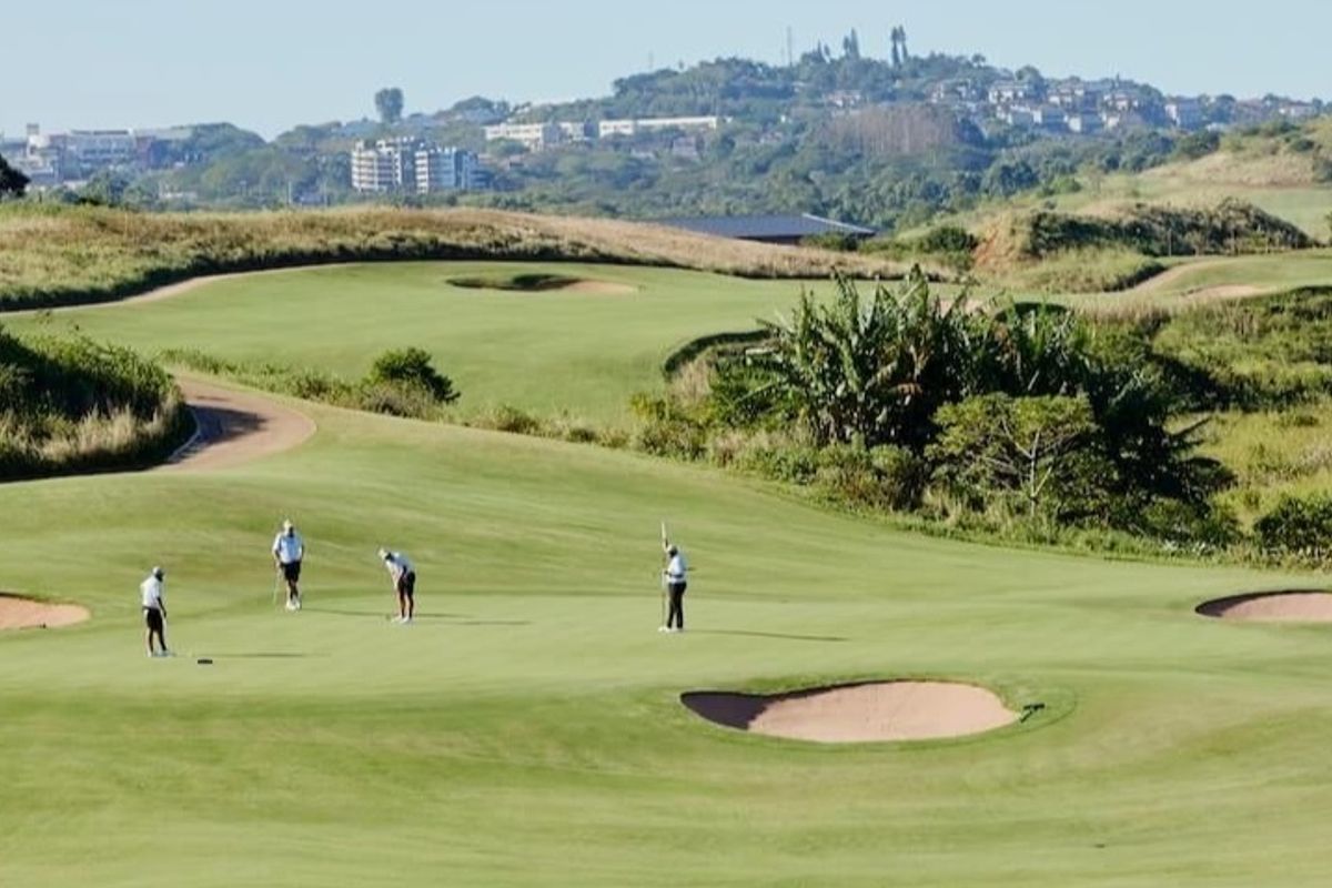 A scenic view of a well-maintained golf course featuring manicured fairways and sand bunkers, set against a backdrop of rolling hills and distant development.