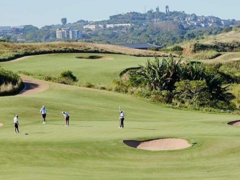 A scenic view of a well-maintained golf course featuring manicured fairways and sand bunkers, set against a backdrop of rolling hills and distant development.