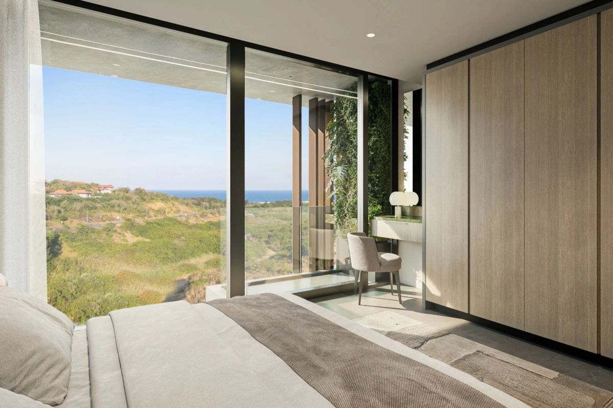 Modern bedroom featuring floor-to-ceiling windows with expansive coastal views, built-in timber-finish wardrobes, and an integrated vanity area.