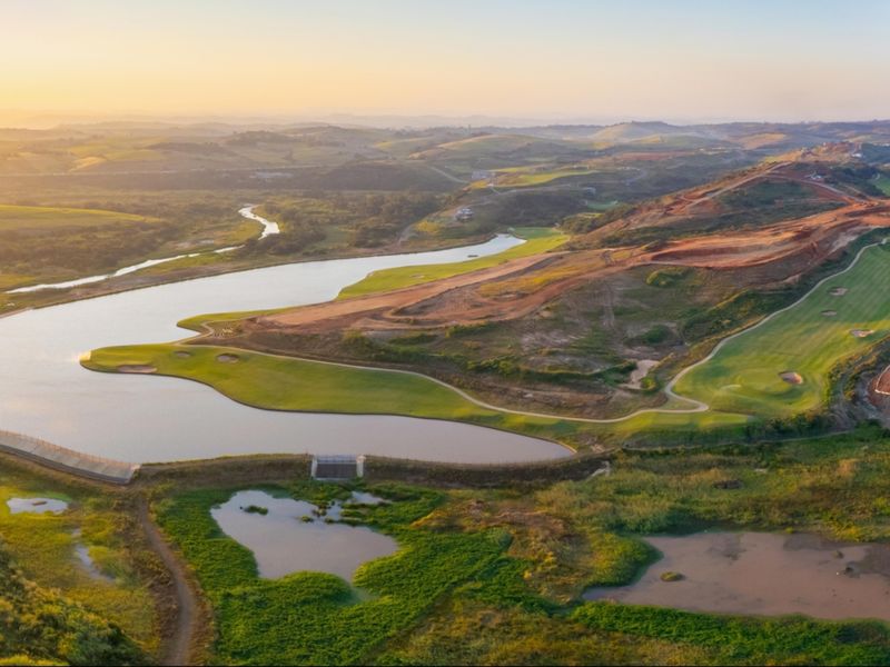 Aerial view of a sprawling golf course landscape featuring a large dam and rolling hills at sunset.