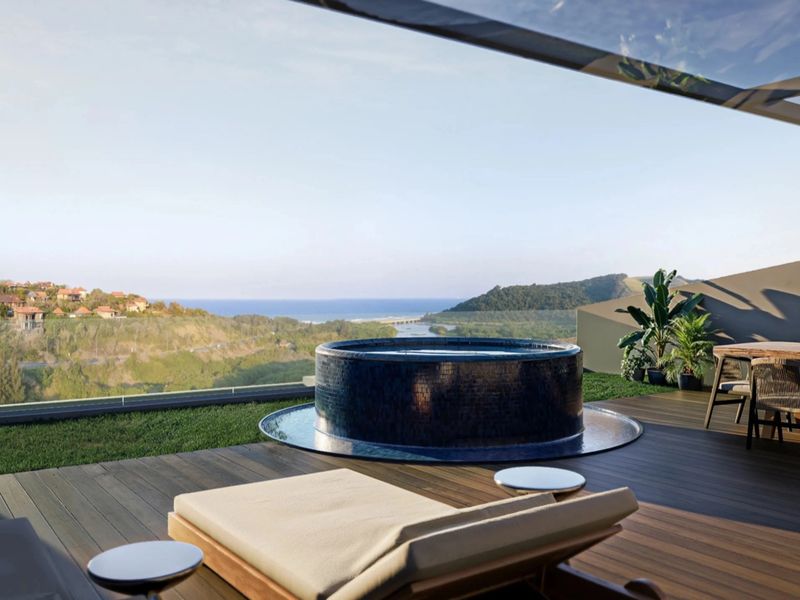 Spacious penthouse balcony featuring a built-in circular jacuzzi, timber decking, and glass balustrades with panoramic coastal and landscape views.