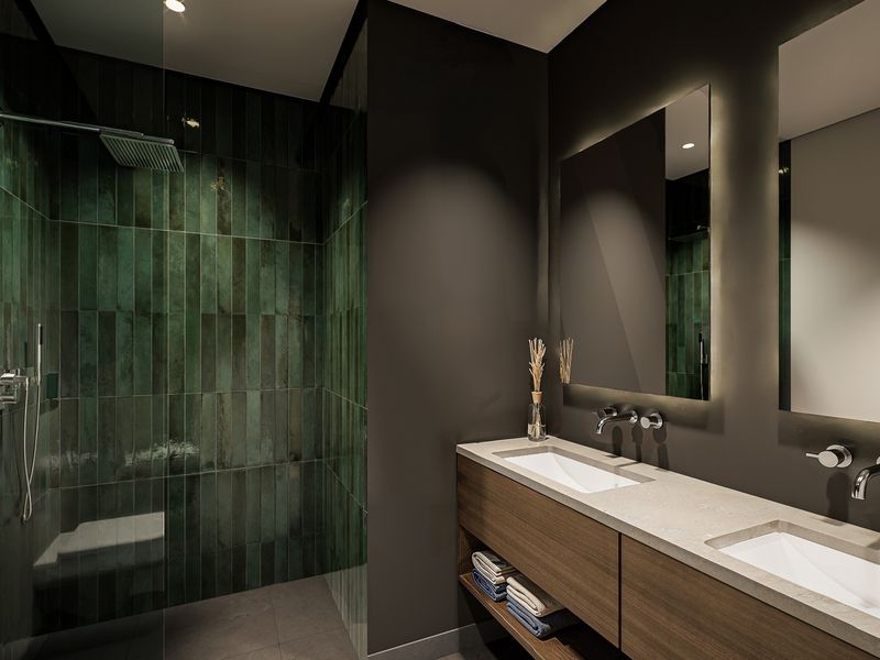 Modern luxury bathroom featuring a double vanity with stone countertop, wall-mounted faucets, backlit mirrors, and a spacious walk-in shower with green feature tiling.