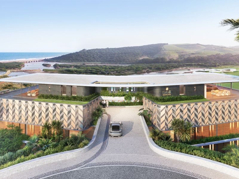 An aerial perspective of a modern architectural development featuring a paved driveway, green roof elements, and scenic coastal landscape views.