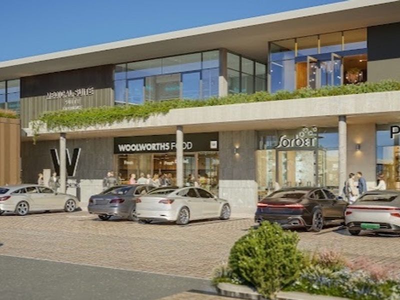 A modern commercial retail center featuring paved parking, landscaped garden beds, and multiple storefronts with a contemporary architectural design.
