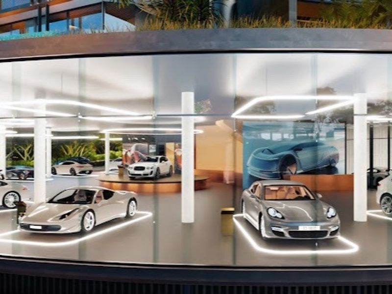 A modern, high-end luxury garage featuring a curved glass facade, structural columns, and integrated floor lighting for vehicle display.