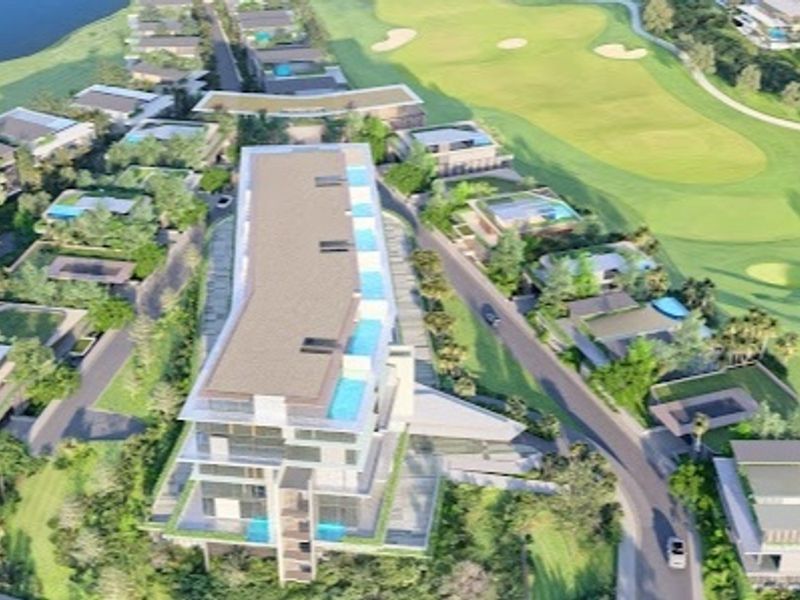 An aerial view of a residential development situated adjacent to a golf course, featuring multiple buildings and swimming pools.
