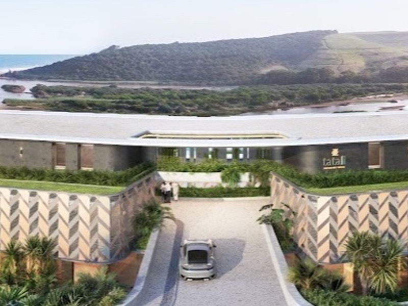 An aerial perspective of a modern architectural property featuring a unique roof design and landscaped elements, overlooking a coastal landscape.