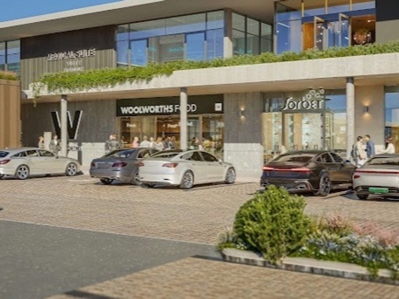 Modern commercial retail center exterior featuring paved parking, glass storefronts, and landscaped architectural elements.