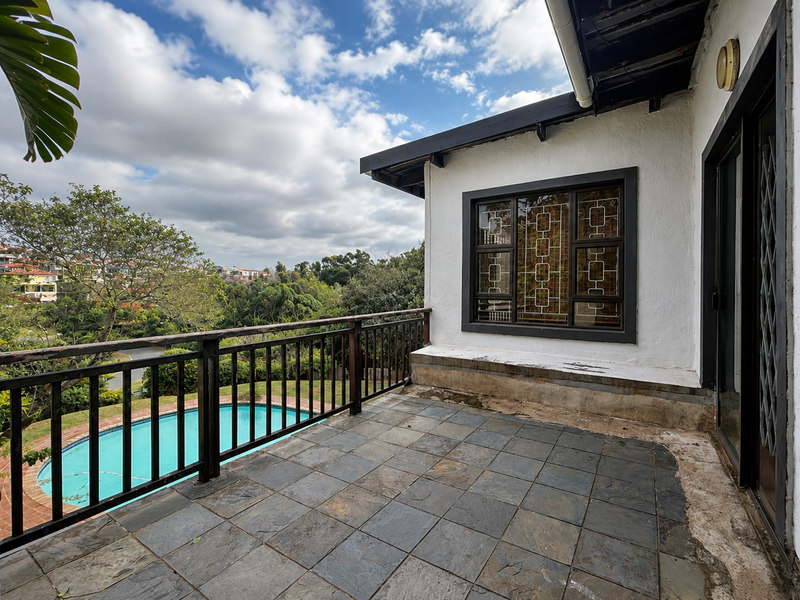 Covered balcony featuring slate tile flooring, wooden balustrade, and views over the swimming pool and surrounding neighborhood.