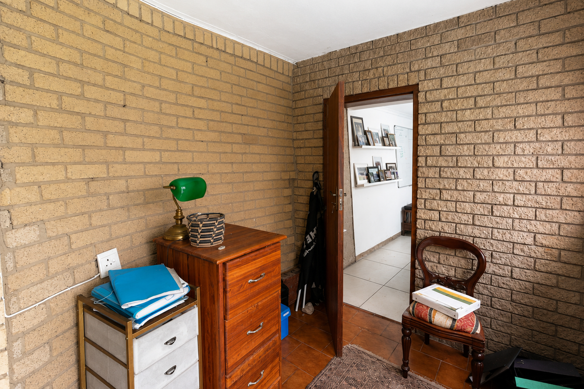 A bedroom featuring exposed brick walls and tiled flooring, with a doorway leading into an adjacent hallway.