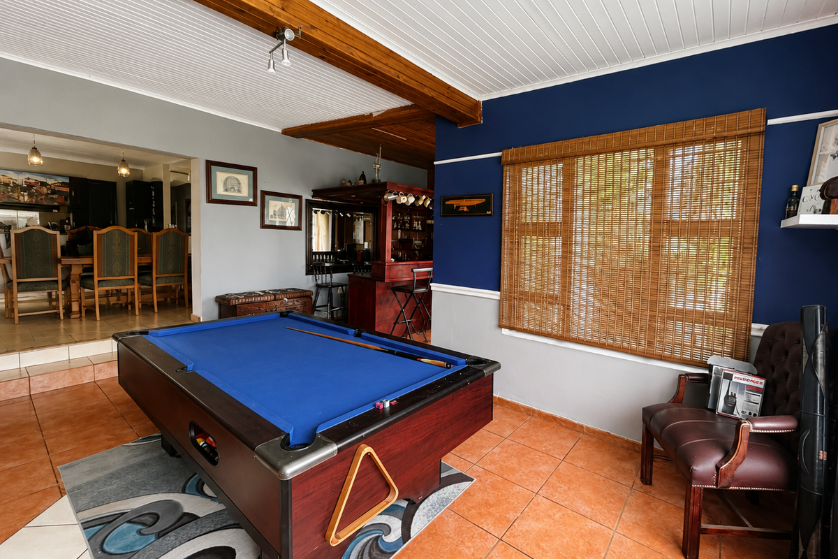Spacious living area featuring exposed timber ceiling beams, tiled flooring, and a built-in bar, with an adjacent dining space visible.