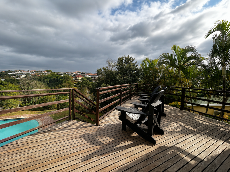 Elevated timber deck featuring a wooden balustrade, overlooking a swimming pool and surrounding landscape.
