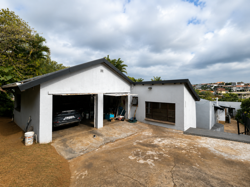 Front exterior view of a house featuring a double garage and a concrete driveway with visible weathering and cracking.