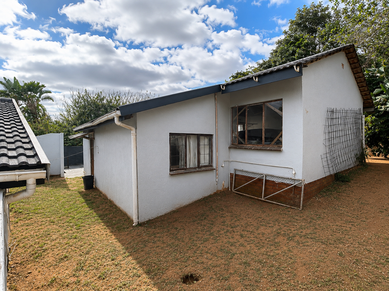 Rear exterior view of the house featuring a tiled roof, white rendered walls, and metal-framed windows set against a garden area.