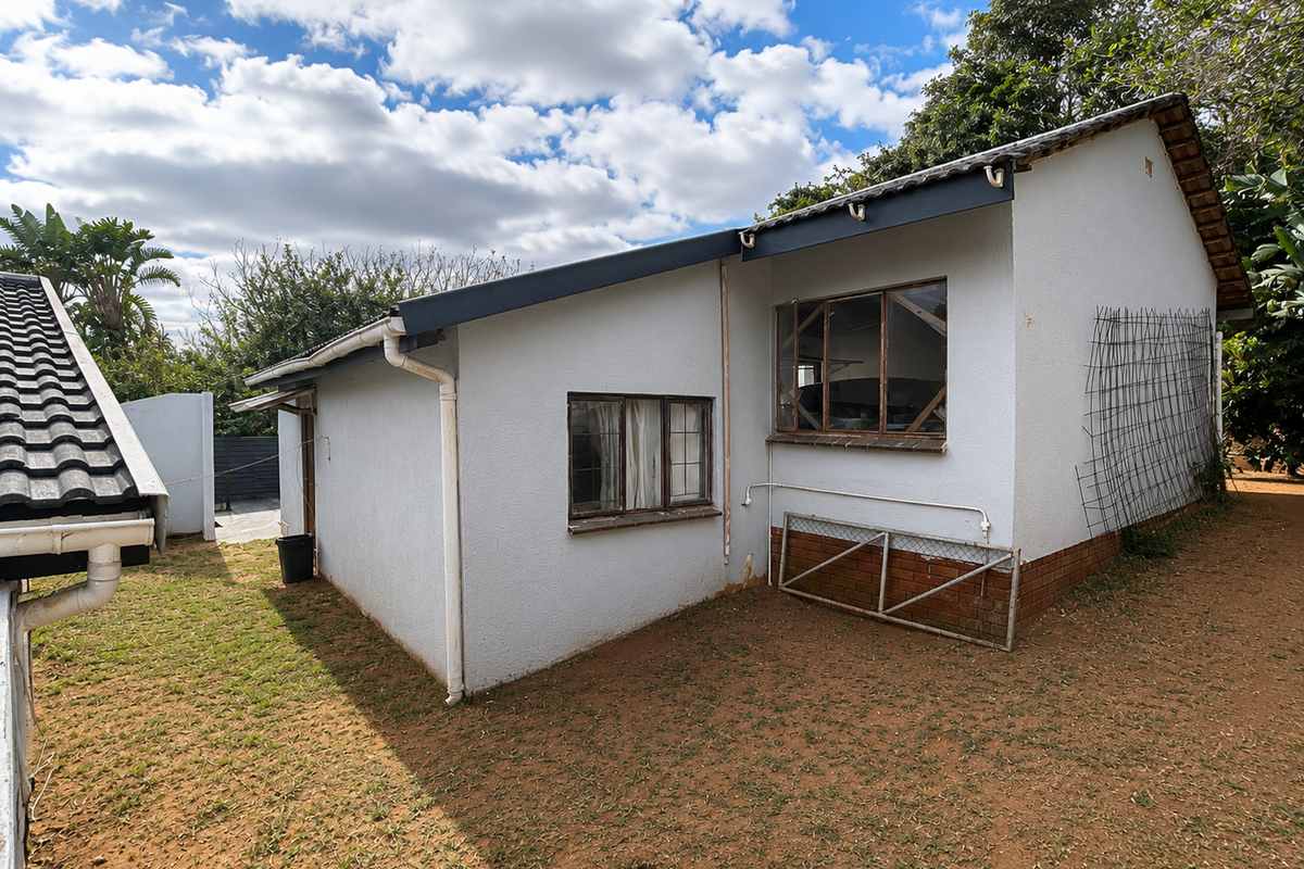 Rear exterior view of the house featuring a tiled roof, white rendered walls, and metal-framed windows set against a garden area.