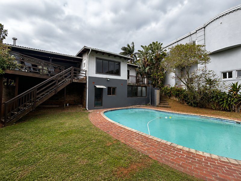 Rear exterior view featuring a swimming pool with brick paving, a raised wooden deck, and a staircase leading to the upper level.