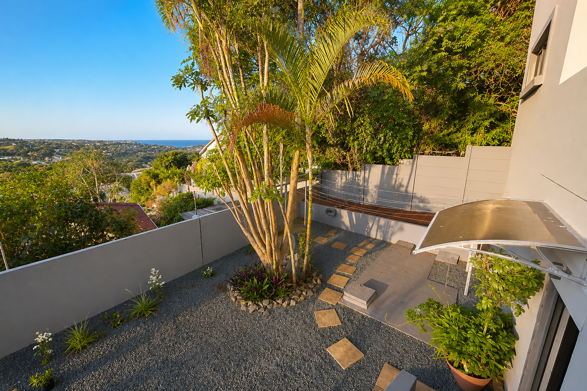 A well-maintained rear courtyard featuring gravel landscaping, stepping stones, a boundary wall, and a protective awning, offering elevated views of the surrounding area.
