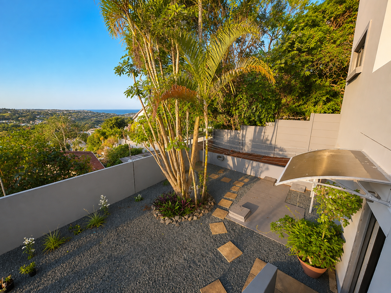 A well-maintained rear courtyard featuring gravel landscaping, stepping stones, a boundary wall, and a protective awning, offering elevated views of the surrounding area.