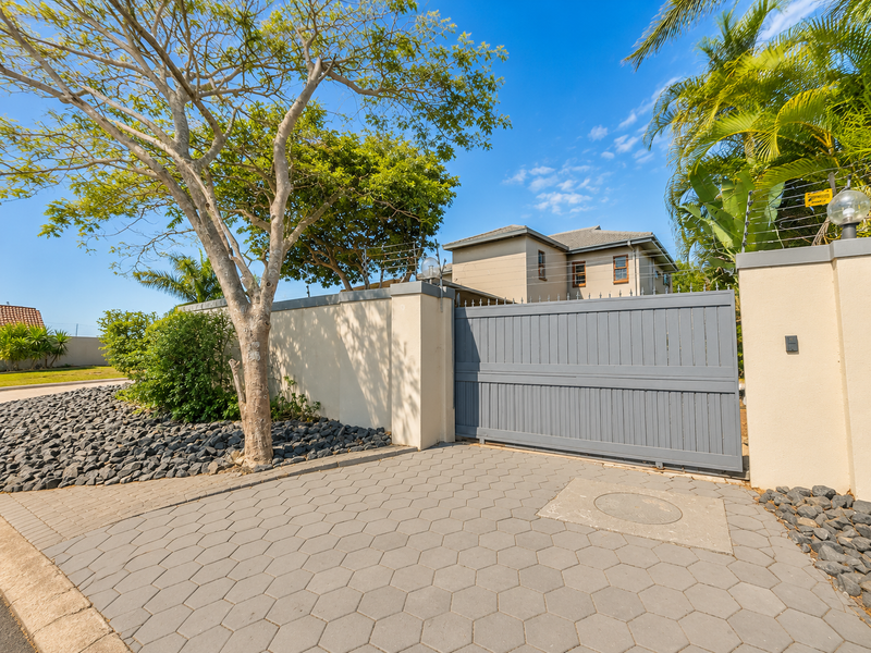 Front entrance view featuring a modern grey sliding gate, secure perimeter wall with electric fencing, and a paved driveway.