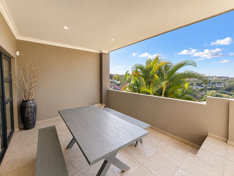 A covered balcony featuring tiled flooring, recessed lighting, and a low-wall balustrade, offering an open-air space with scenic views.