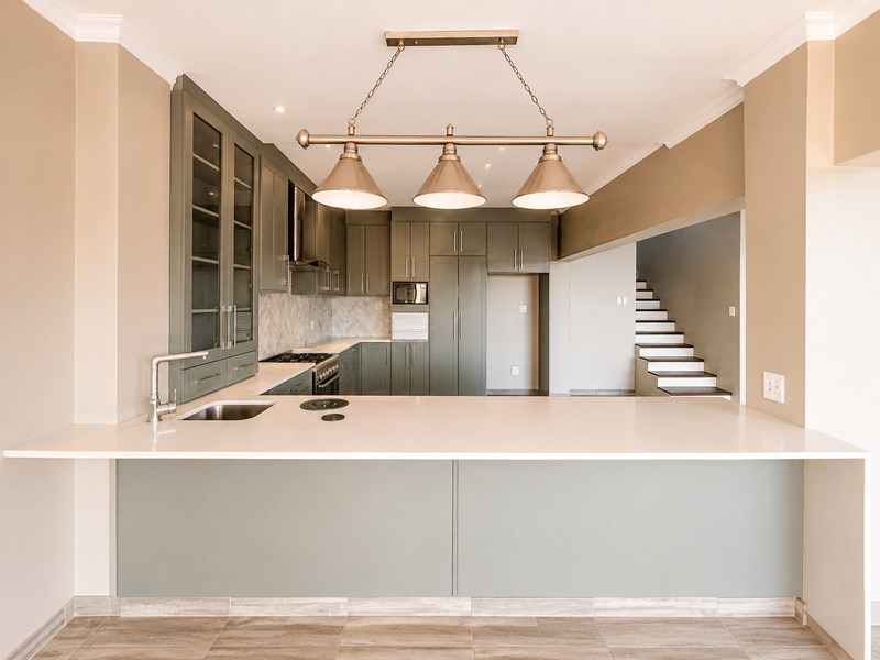 Modern kitchen featuring sage green cabinetry, quartz countertops, herringbone backsplash, built-in appliances, and stylish pendant lighting, with an open-plan layout and adjacent staircase.