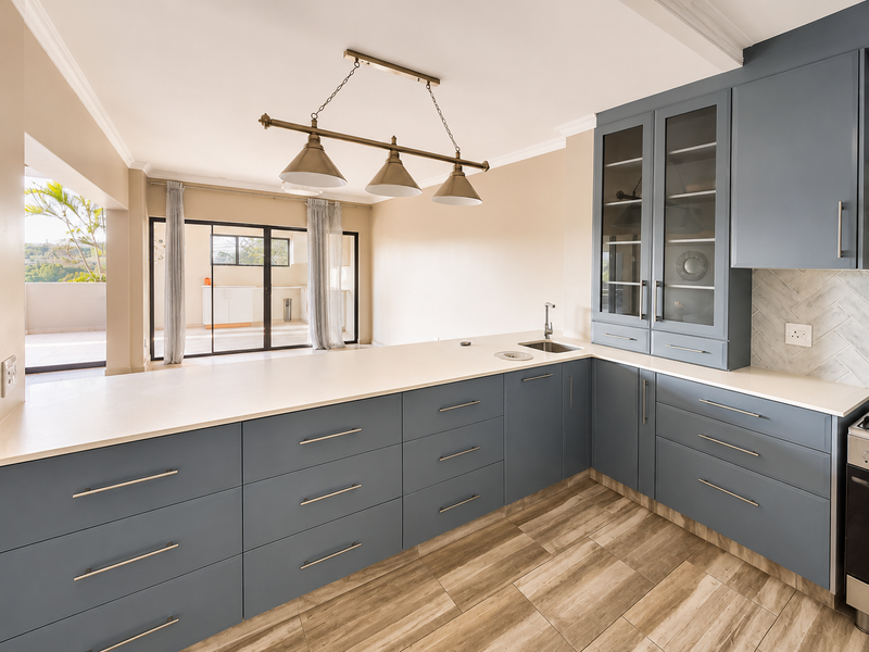 Modern kitchen featuring blue cabinetry, stone countertops, herringbone backsplash, and wood-look tile flooring, with seamless flow to an outdoor patio area.