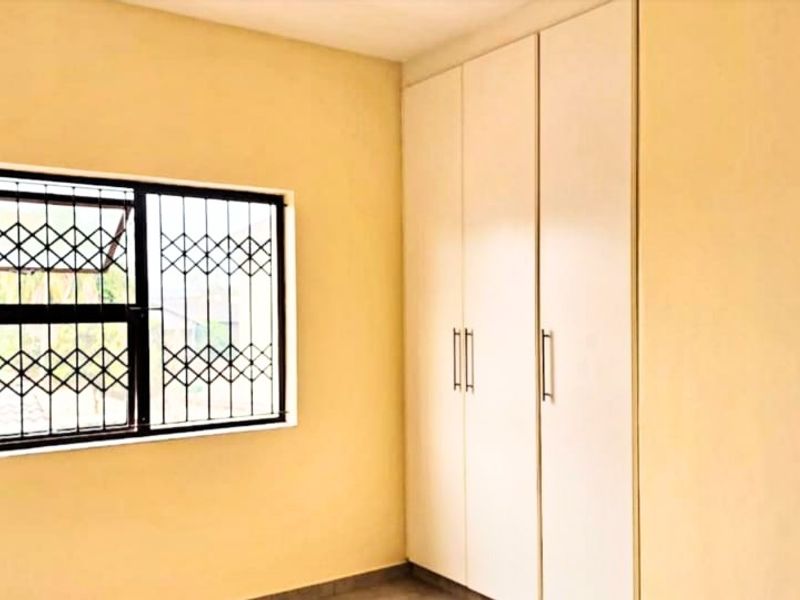 A clean, empty bedroom featuring neutral walls, tiled flooring, and built-in cupboards with security burglar bars on the window.