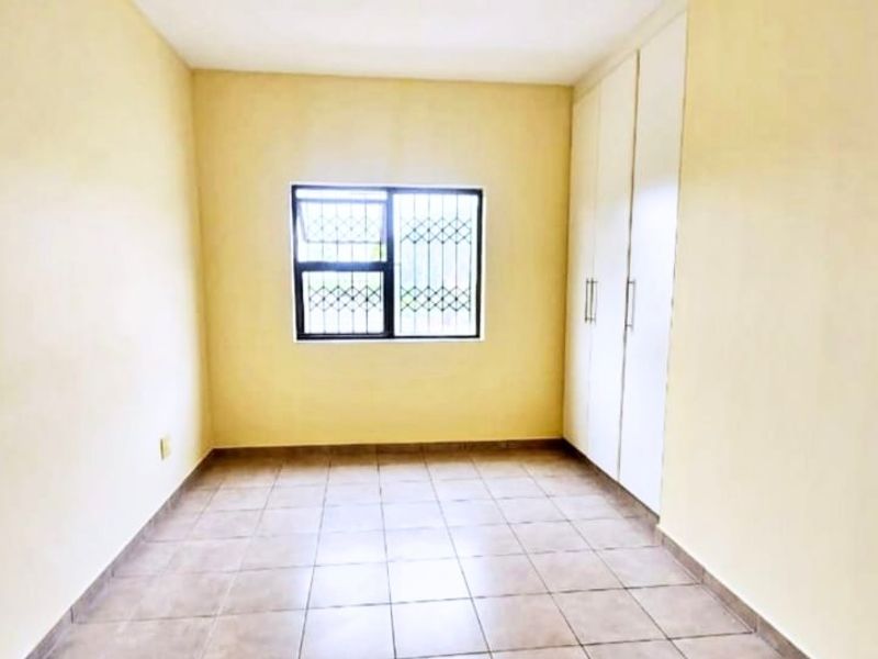 An empty bedroom featuring tiled flooring, built-in cupboards, and a window fitted with security bars.
