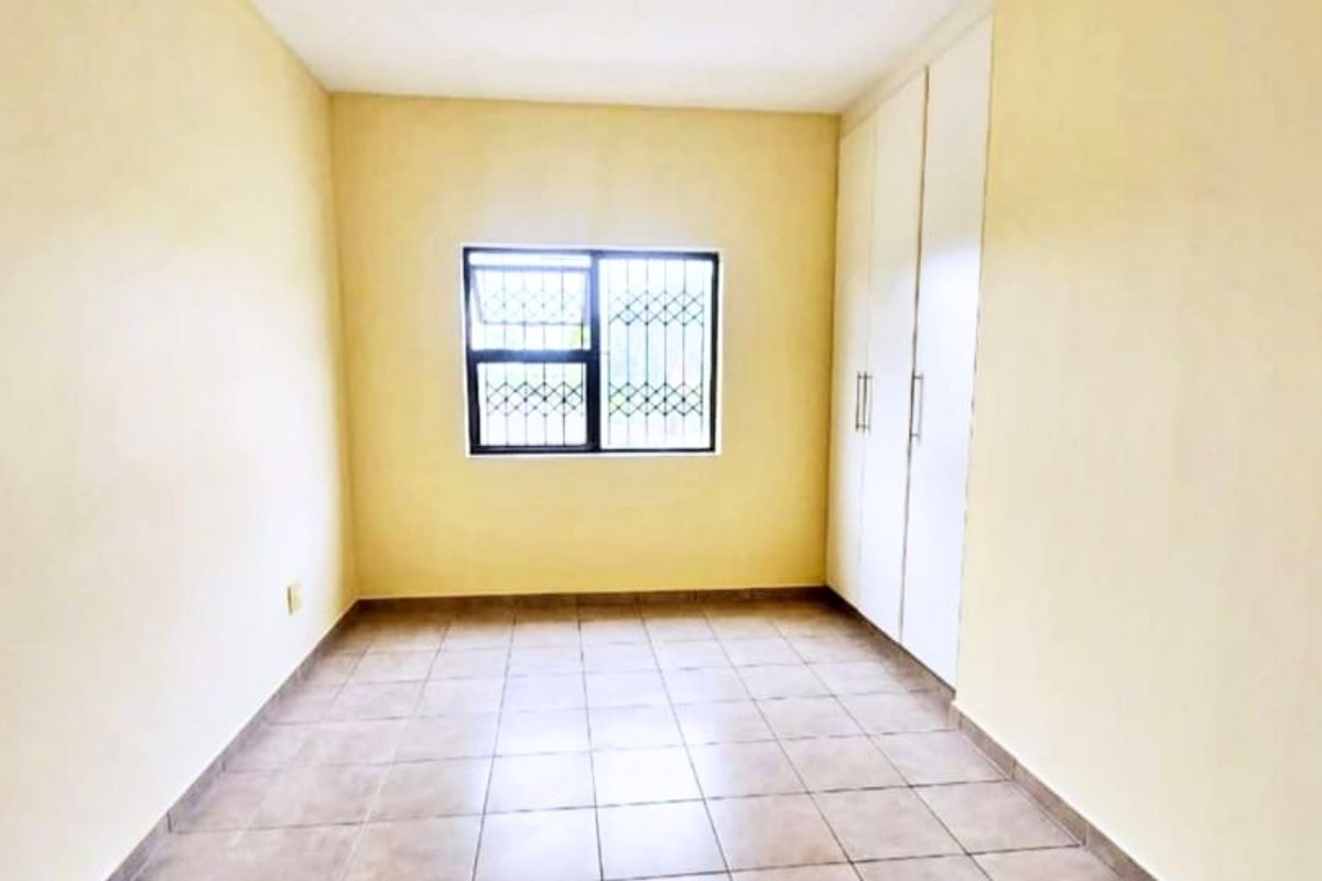 An empty bedroom featuring tiled flooring, built-in cupboards, and a window fitted with security bars.