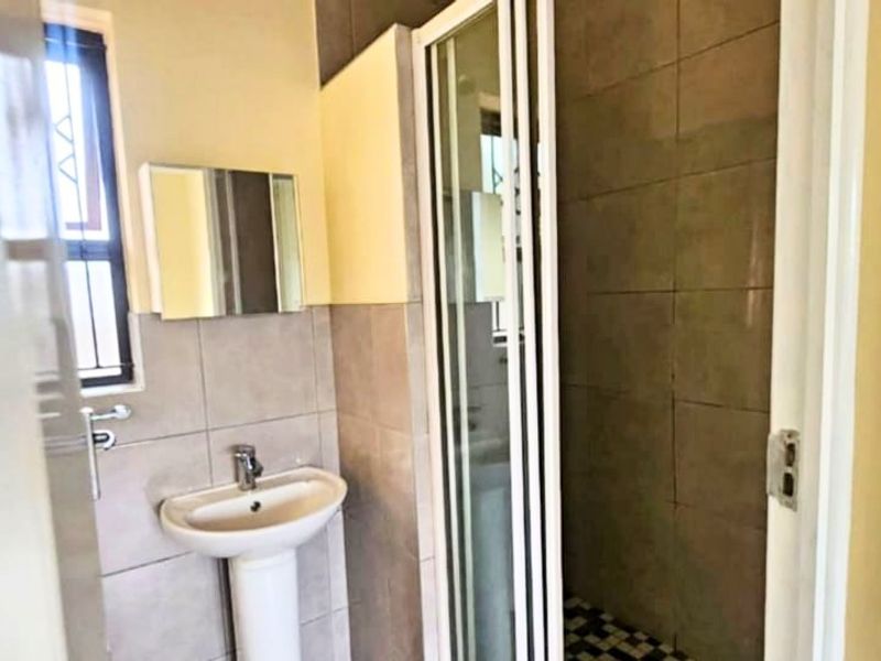 A functional bathroom featuring a pedestal basin, tiled walls, and a separate shower enclosure with a folding door.