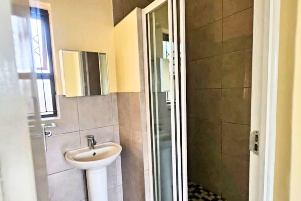 A functional bathroom featuring a pedestal basin, tiled walls, and a separate shower enclosure with a folding door.