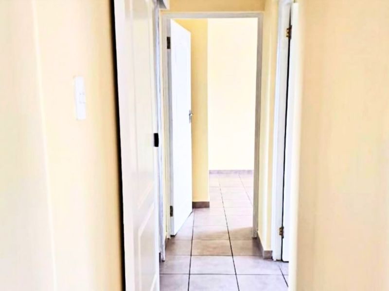 A simple, empty hallway with tiled flooring connecting to other rooms in the apartment.