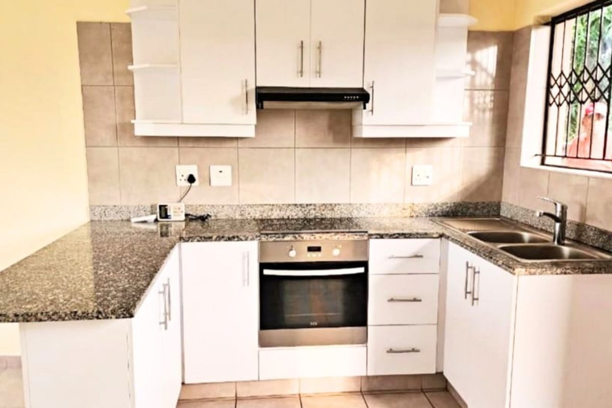 A functional kitchen featuring white cabinetry, granite countertops, a built-in oven with hob, extractor fan, and a double basin sink with tiled backsplash.