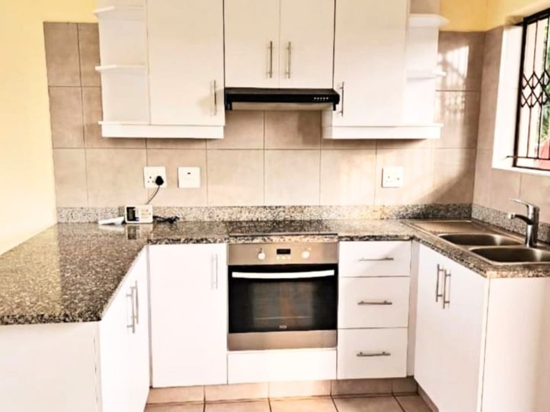 A functional kitchen featuring white cabinetry, granite countertops, a built-in oven with hob, extractor fan, and a double basin sink with tiled backsplash.