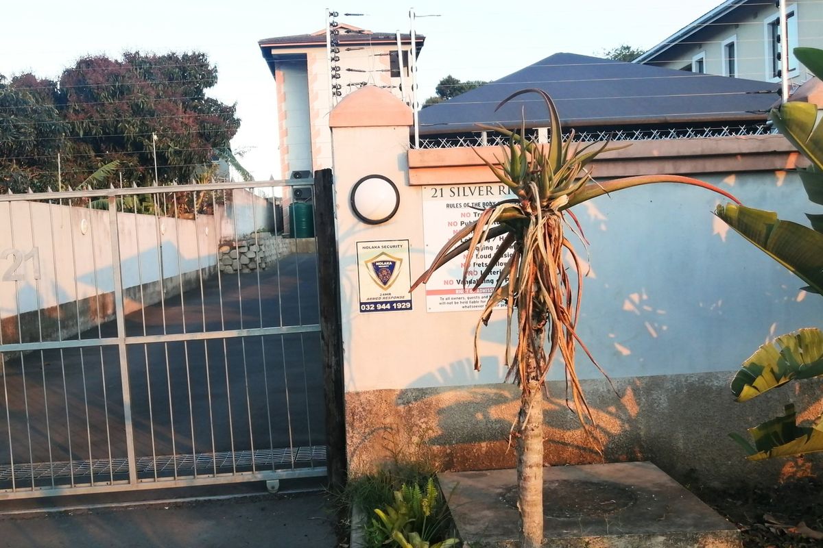 Front entrance view of the apartment complex featuring a secure gated driveway, perimeter wall with electric fencing, and security signage.