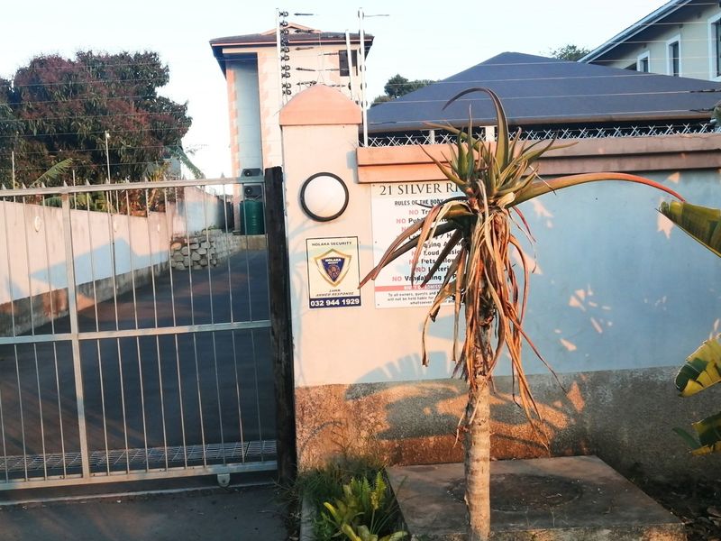 Front entrance view of the apartment complex featuring a secure gated driveway, perimeter wall with electric fencing, and security signage.