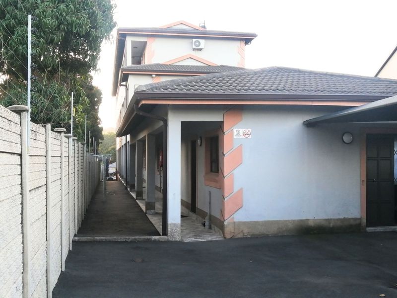 Exterior view of the apartment building featuring a paved driveway, carport, and secure boundary wall with perimeter security.