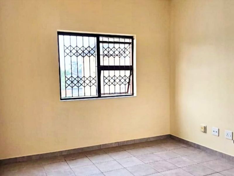 An empty open-plan living area featuring tiled flooring, a window with security bars, and a granite countertop edge.
