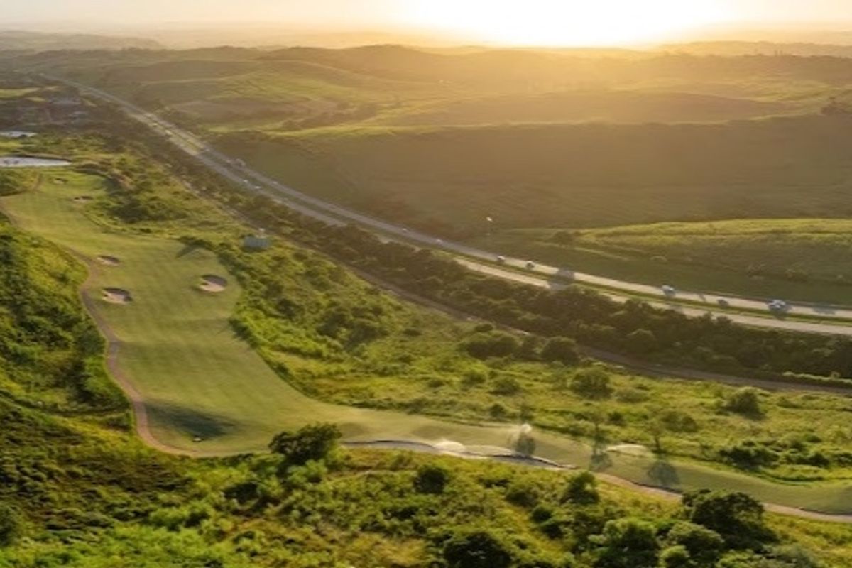 An aerial view of a golf course landscape at sunset, showcasing the rolling terrain and surrounding natural environment.