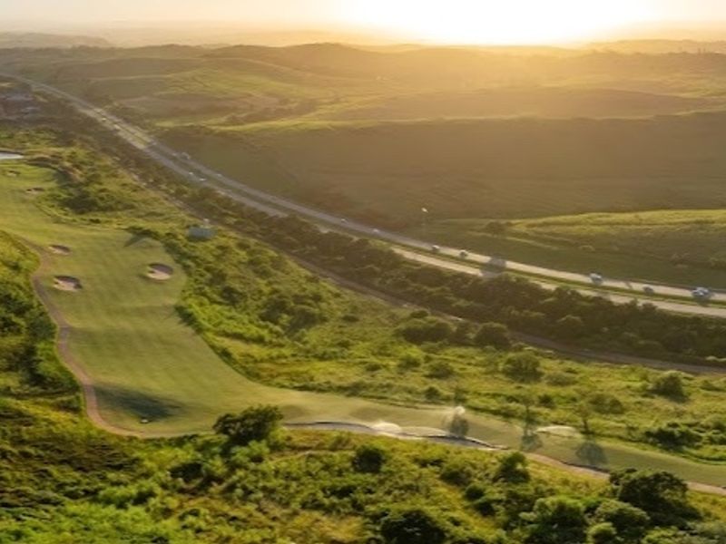 An aerial view of a golf course landscape at sunset, showcasing the rolling terrain and surrounding natural environment.